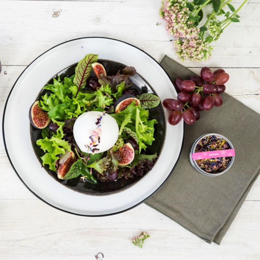 Salat mit Feigen, Trauben und Blütenmix. Runde, silberne Dose mit Blütenmix. Rosa Etikett. Produktname: Blütenmix.