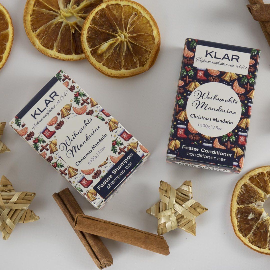 Zwei Klar-Seifen-Verpackungen mit Weihnachtsdesign. Text: Klar, Weihnachtsmandarine, Fester Conditioner, Festes Shampoo. Dekoration.