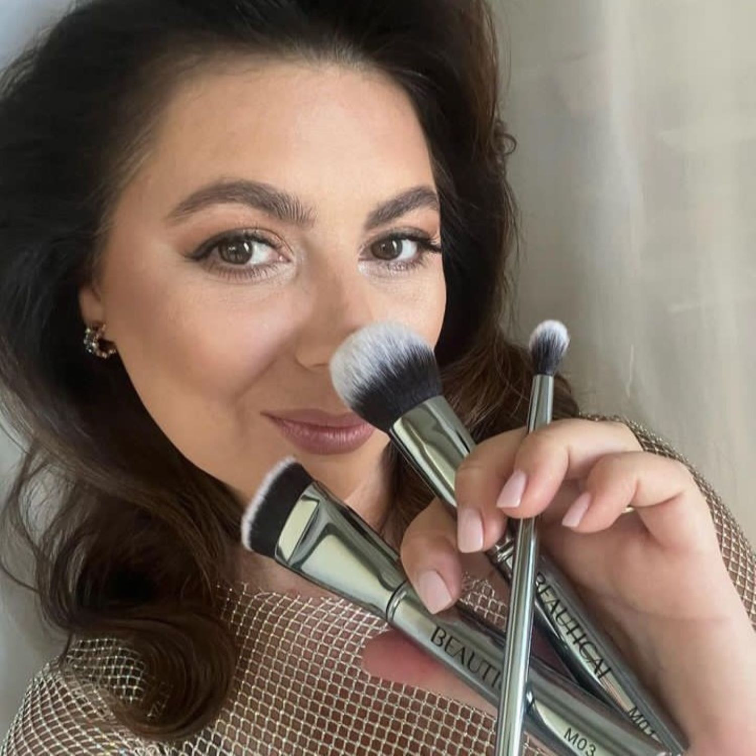 Frau hält drei Pinsel. Die Marke BEAUTICAL ist sichtbar. Silberne Griffe.