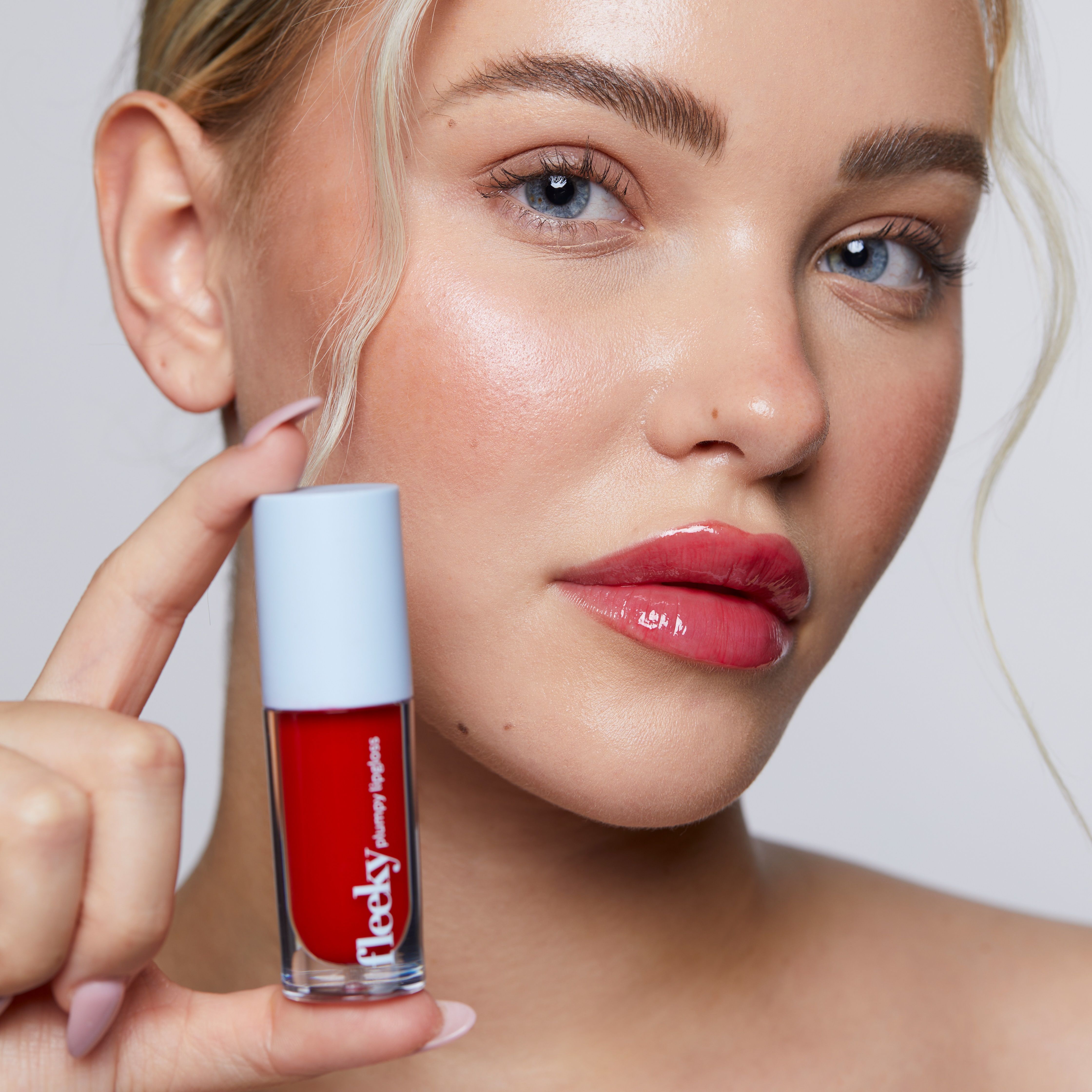 Frau hält eine Flasche roter Lipgloss. Aufschrift: fleeky plumpy lipgloss.