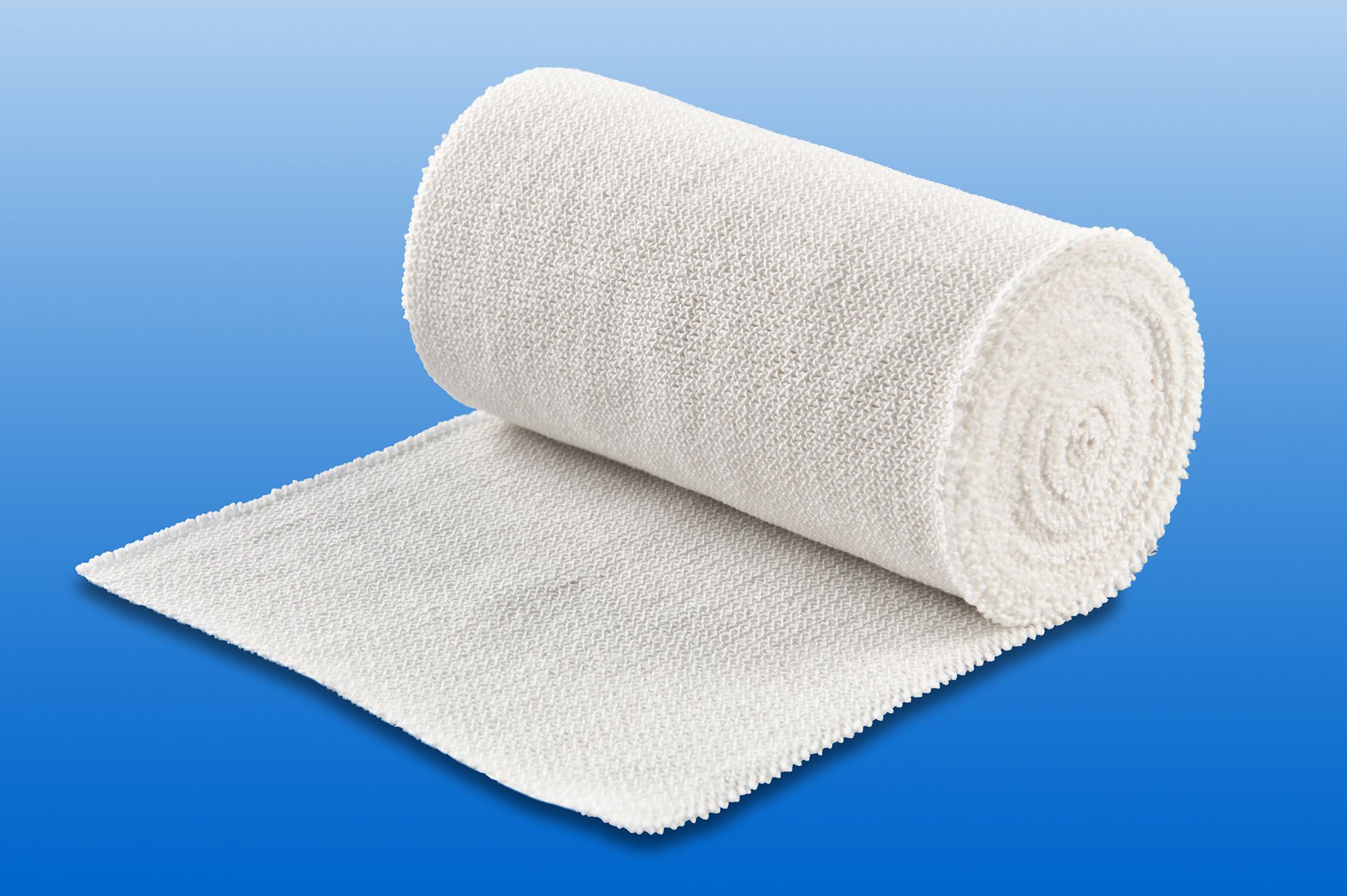 Textilelastische Idealbinde, weiß, gerollt und teilweise abgerollt. Auf blauem Hintergrund.