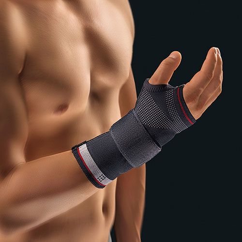 Handgelenkbandage am Handgelenk einer Person. Schwarz mit roten und weißen Akzenten. Klettverschluss. Mesh-Material.