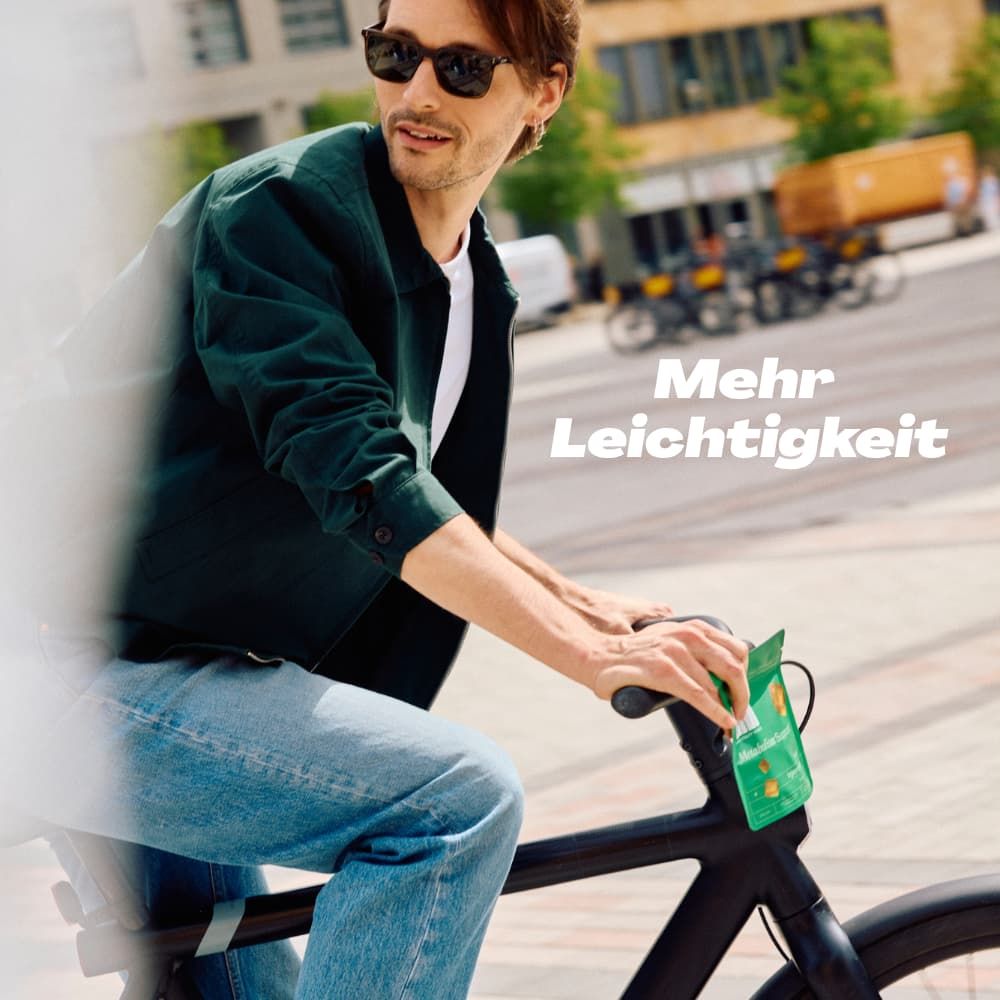 Mann fährt Fahrrad. Auf dem Lenker ist eine kleine grüne Verpackung befestigt. Text: Mehr Leichtigkeit.