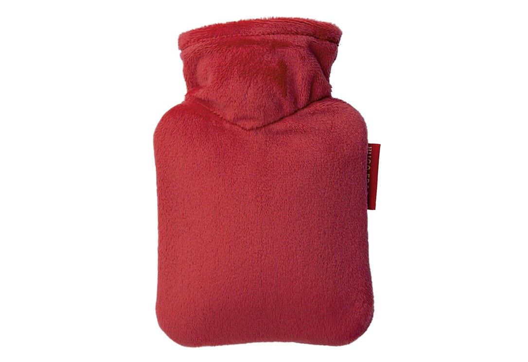 Rote Wärmflasche mit weichem Bezug. Rechteckige Form mit Hals. Kleines rotes Etikett.