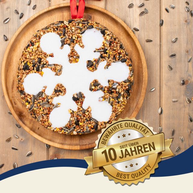 Runder Vogelkuchen auf Holztablett. Schneeflockenmuster. Goldene Plakette: Bewährte Qualität seit über 10 Jahren.