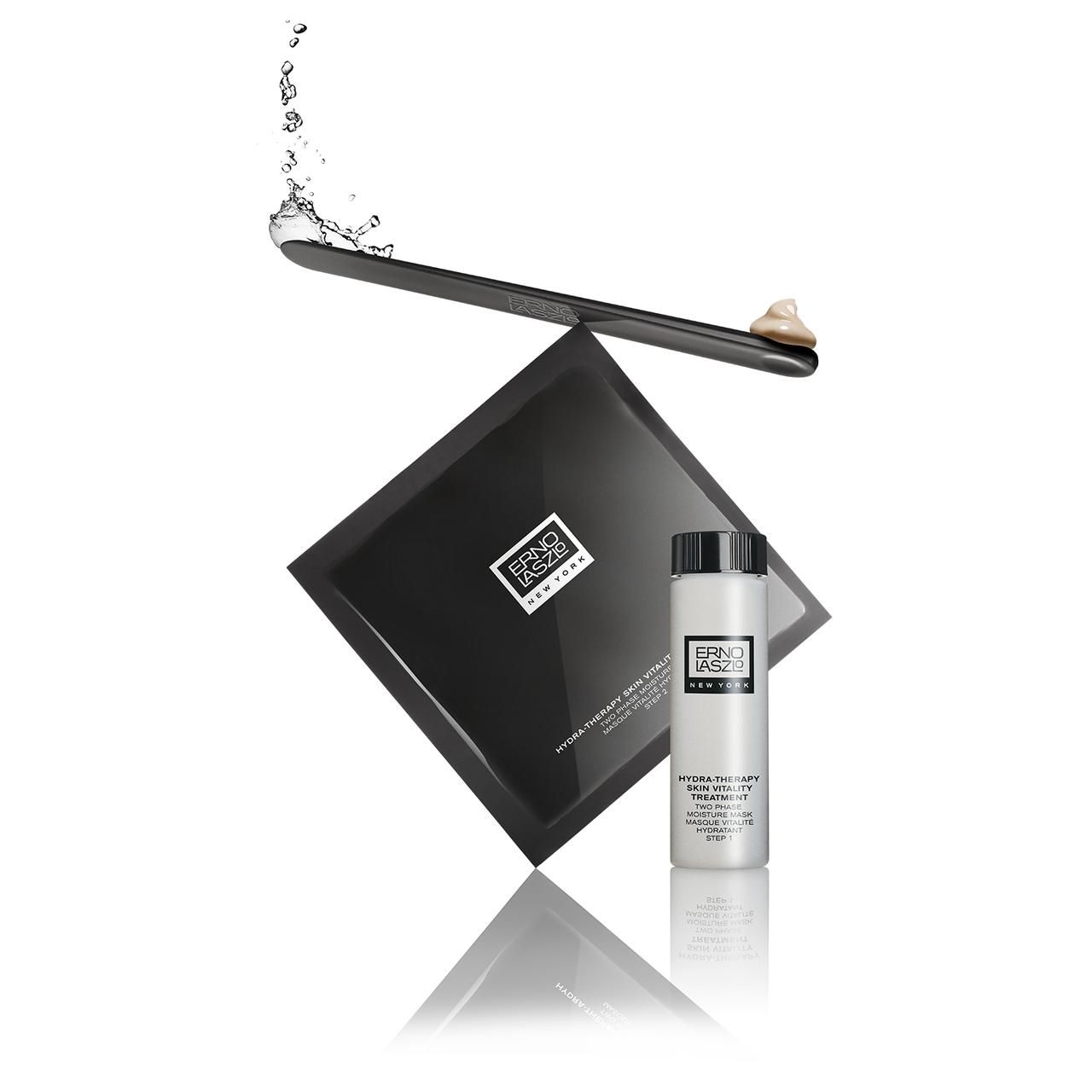 Schwarze Maskenverpackung, Flasche und Spatel. Aufschrift: Erno Laszlo New York. Wasser spritzt. Produktname nicht sichtbar.