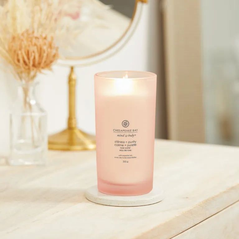 Brennende rosa Kerze. Aufschrift: Chesapeake Bay, mind & body, stillness + purity, calme + pureté, rose water, 355g. Auf Marmorplatte.