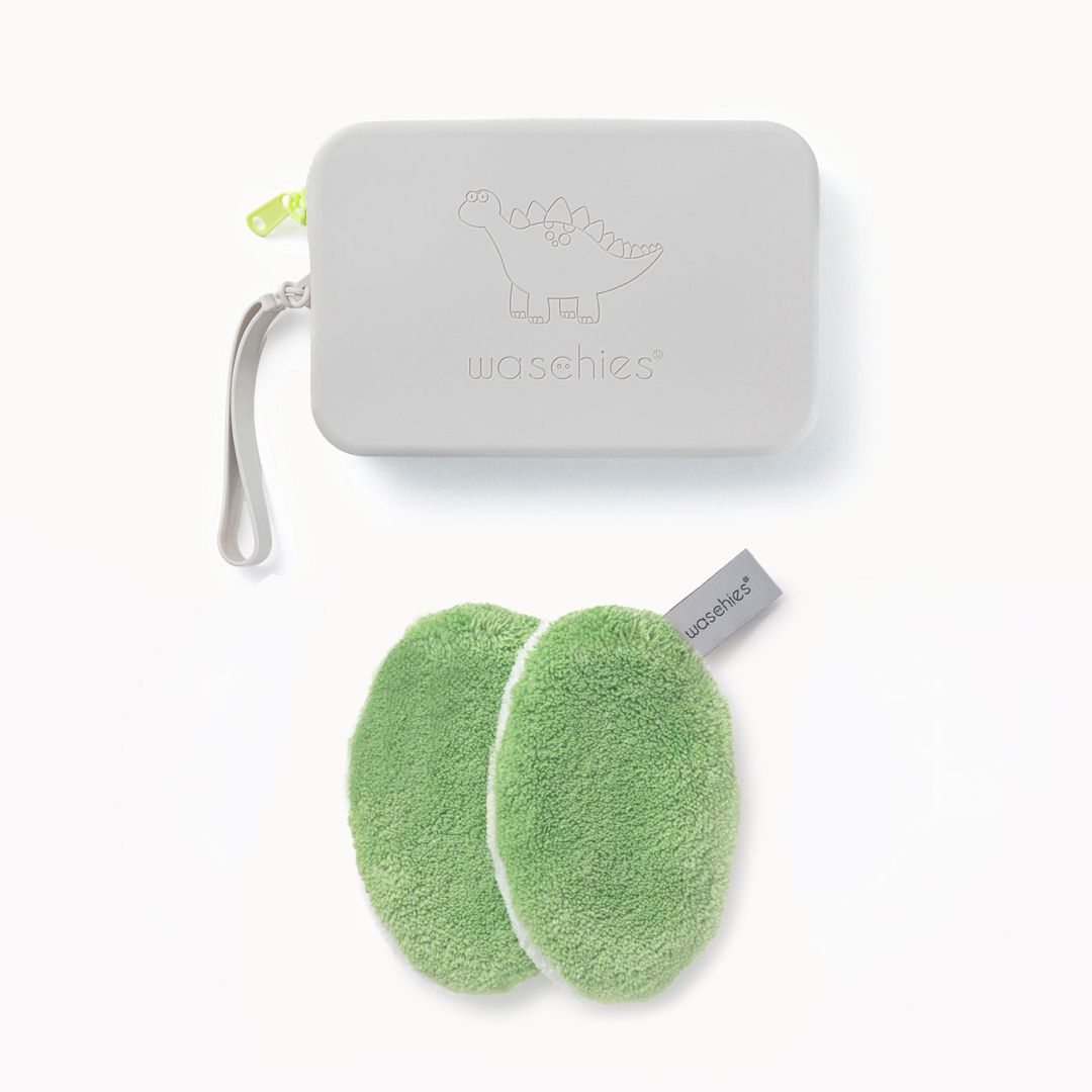 Zwei grüne Waschpads und eine graue Tasche mit Dinosaurier-Motiv. Auf der Tasche steht "waschies".
