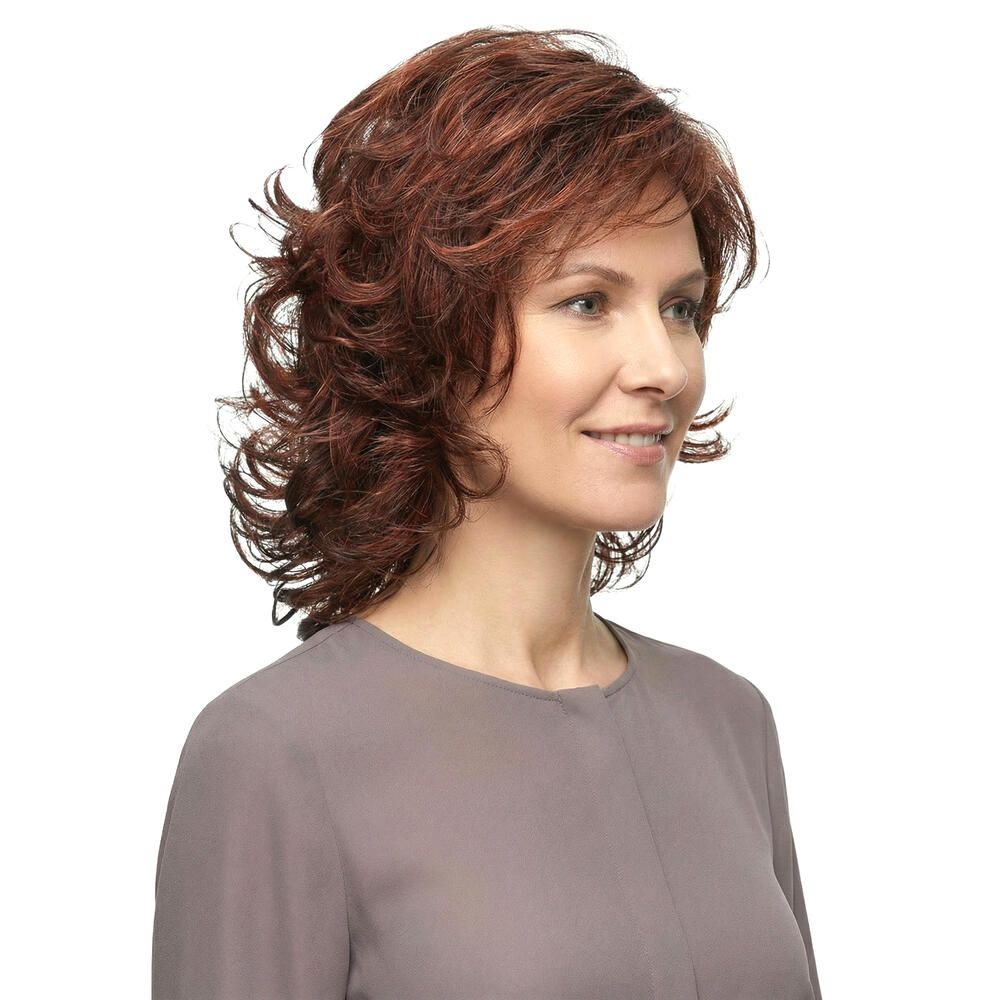 Frau mit rotbrauner, gewellter Perücke, leicht seitlich. Graues Oberteil. Heller Hintergrund.