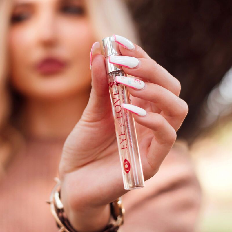 Frau hält einen Parfümflakon. Aufschrift: EYE OF LOVE. Flakon mit Sprühkopf. Hintergrund unscharf.