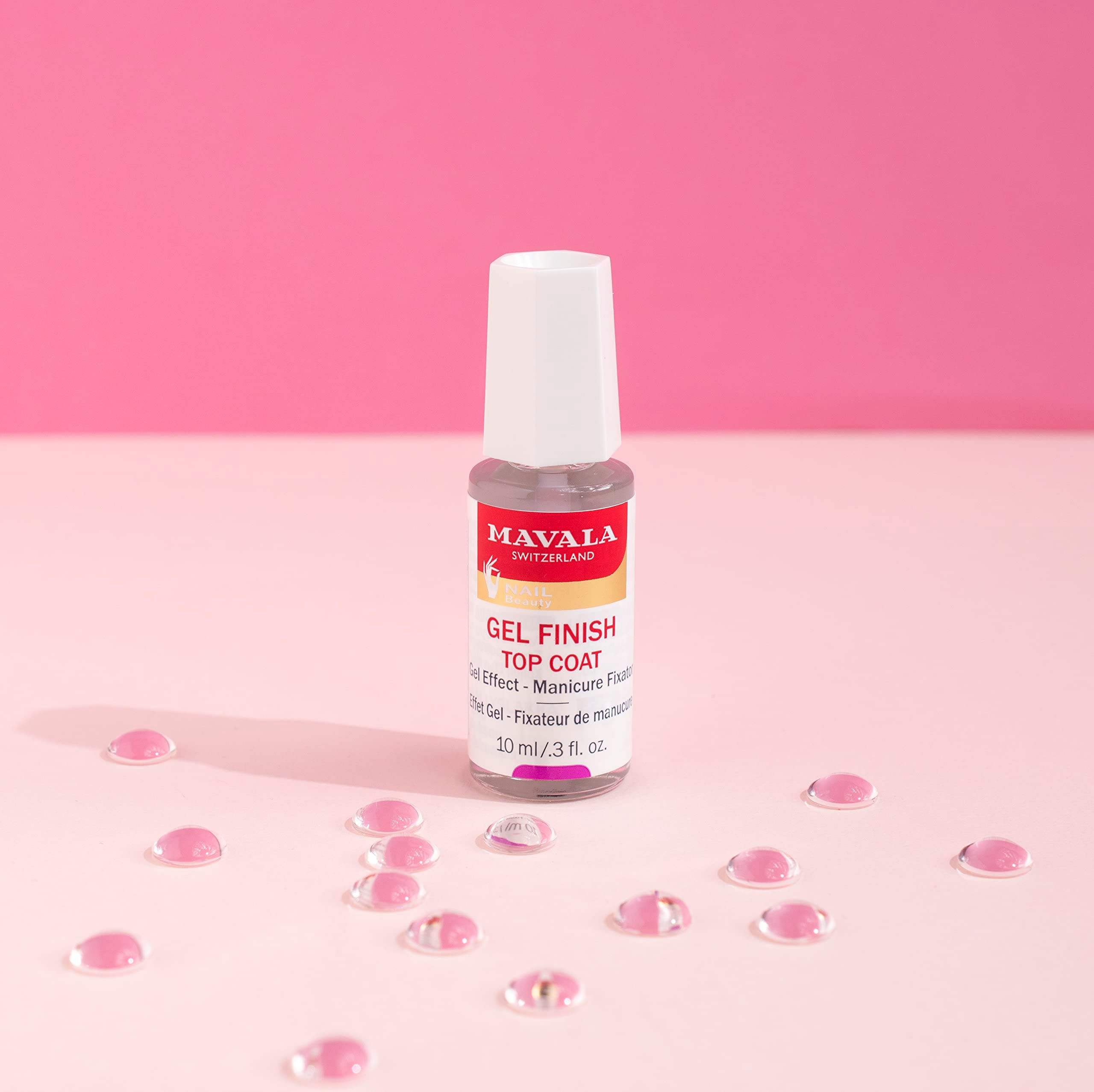 Nagellackflasche mit weißem Deckel. Aufschrift: MAVALA, Gel Finish Top Coat. Rosa Tropfen liegen verstreut.