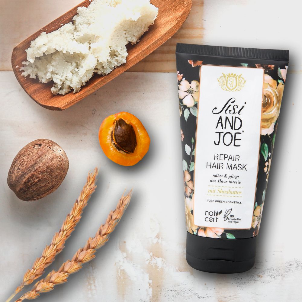 Haarmaske mit Sheabutter, Zutaten auf Holzbrett. Produktverpackung mit floralem Muster und Logo.