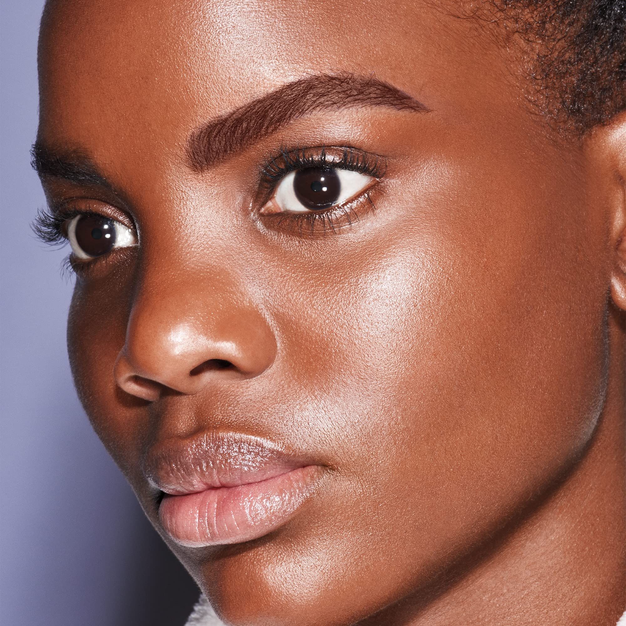 Nahaufnahme eines Gesichts. Dunkle Haut, dunkle Augenbrauen, dunkle Augen. Haut glänzend.
