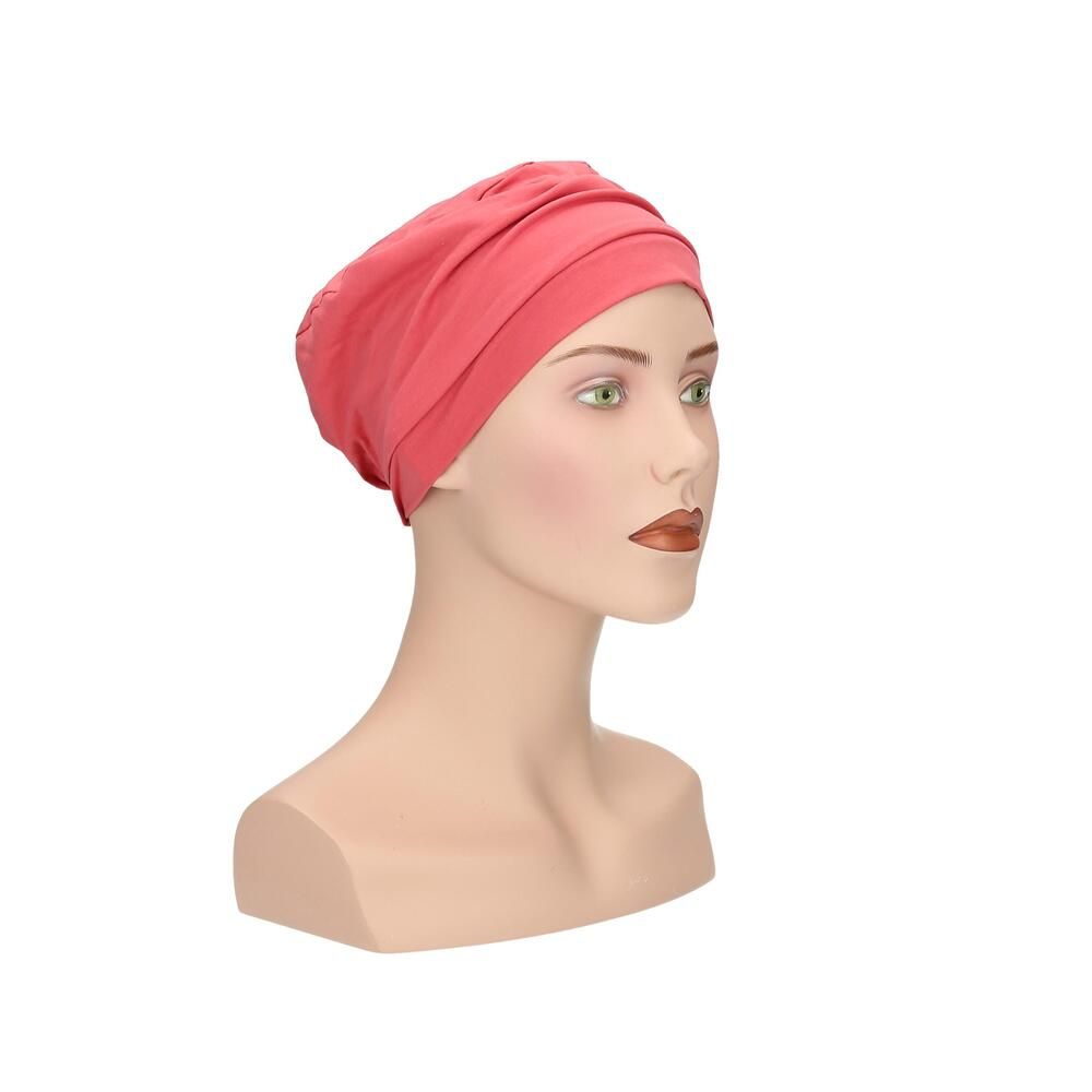 Korallenfarbener Turban auf Büste. Stoffhaube mit Faltenwurf. Schräge Ansicht.