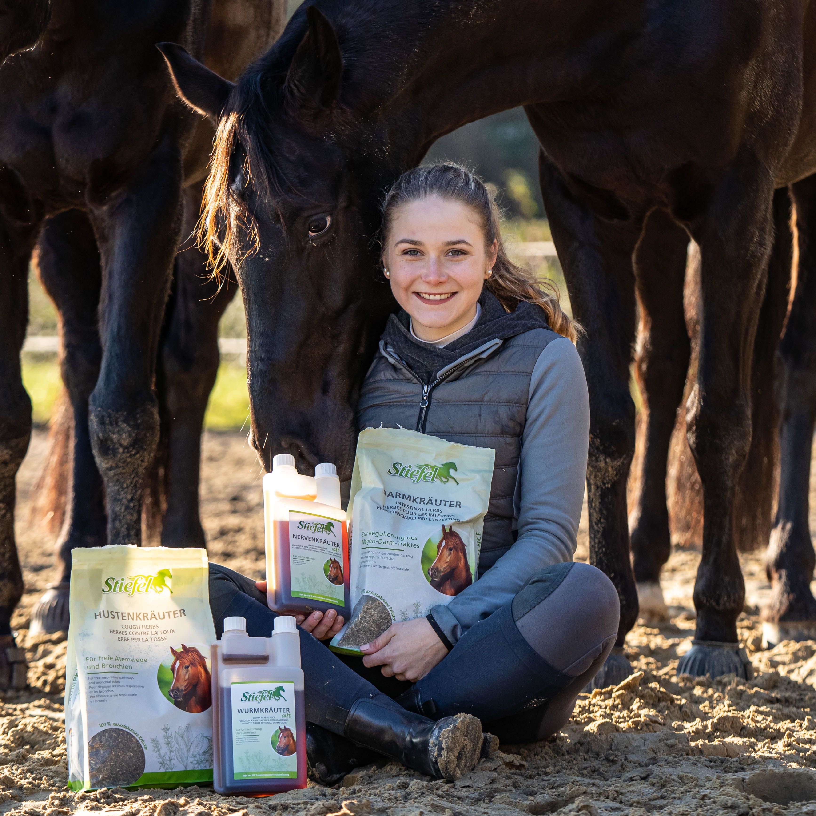Person sitzt mit Produkten. Doppelkammerflasche und Beutel mit Aufschrift: Stiefel Wurmkräuter. Auf dem Beutel ist ein Pferd abgebildet.