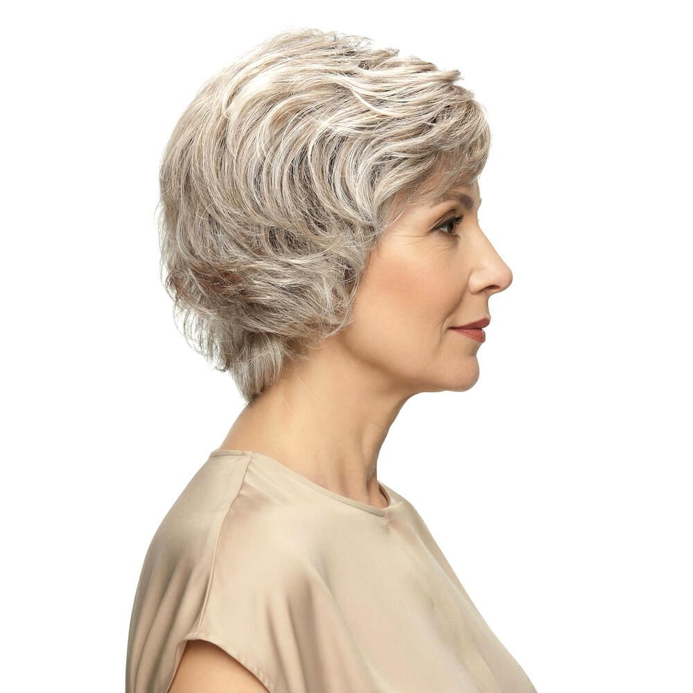Kurzhaarperücke mit grauen Strähnen. Seitenansicht einer Frau mit beigem Oberteil. Frisur mit Volumen.