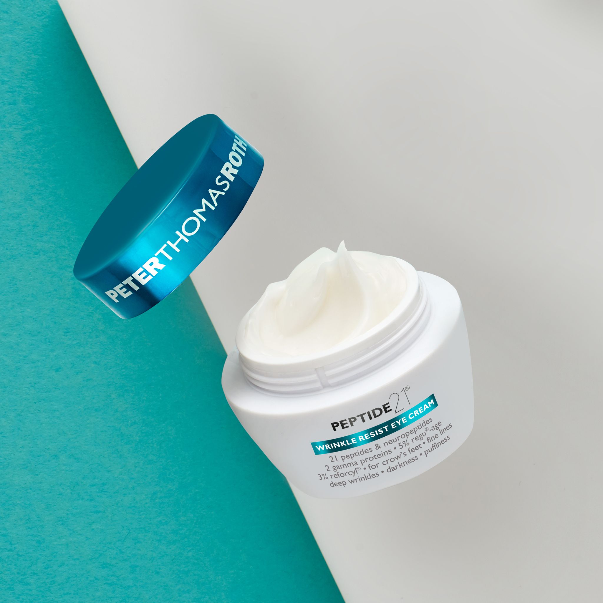 Peter Thomas Roth Peptide 21® Wrinkle Resist Eye Cream. Geöffneter Tiegel, Creme und Deckel. Auf blau-weißem Hintergrund.