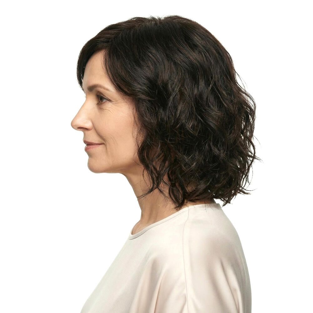 Perücke Capri, braun, gewellt. Frau im Profil, Blick nach links. Helles Oberteil.