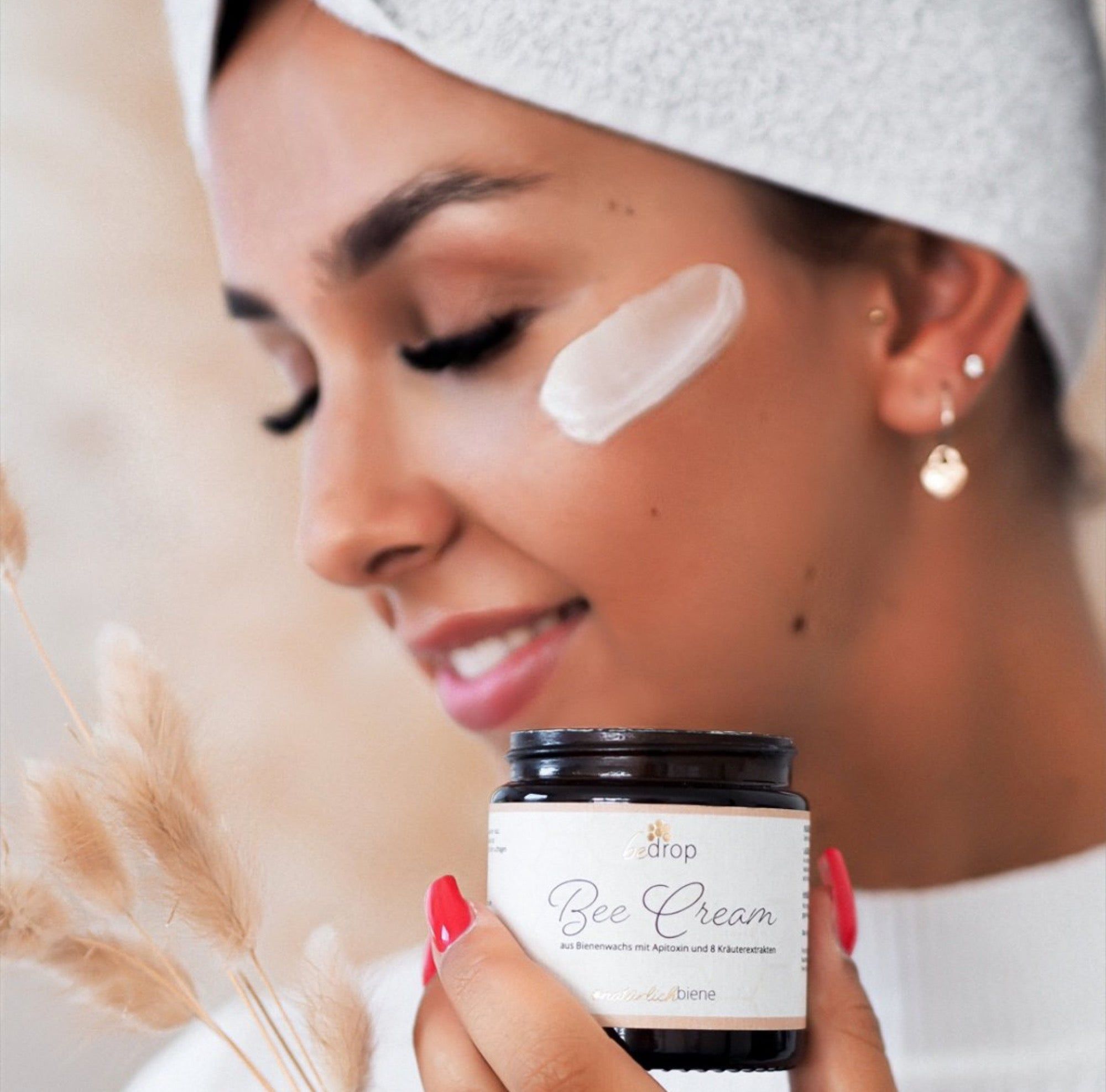 Frau mit Creme auf der Wange. Sie hält einen Tiegel "Bee Cream". Auf dem Tiegel steht "bedrop" und "Bee Cream".
