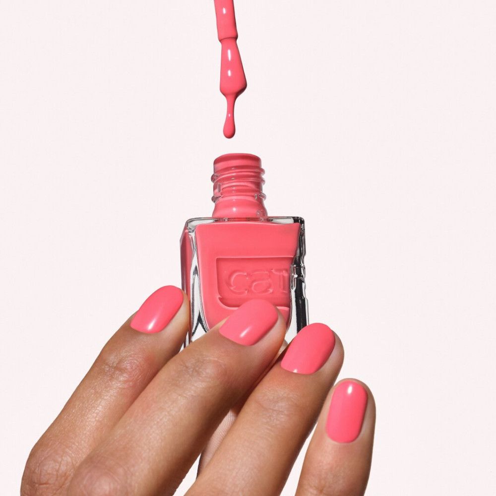 Eine Hand mit korallenrotem Nagellack hält eine Flasche Nagellack. Ein Pinsel tropft Farbe.