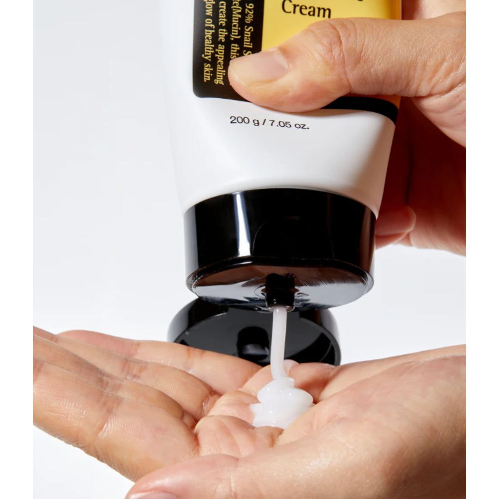 Weiß-schwarze Tube, Produkt wird in Hand gedrückt. Aufschrift: 200 g / 7.05 oz.