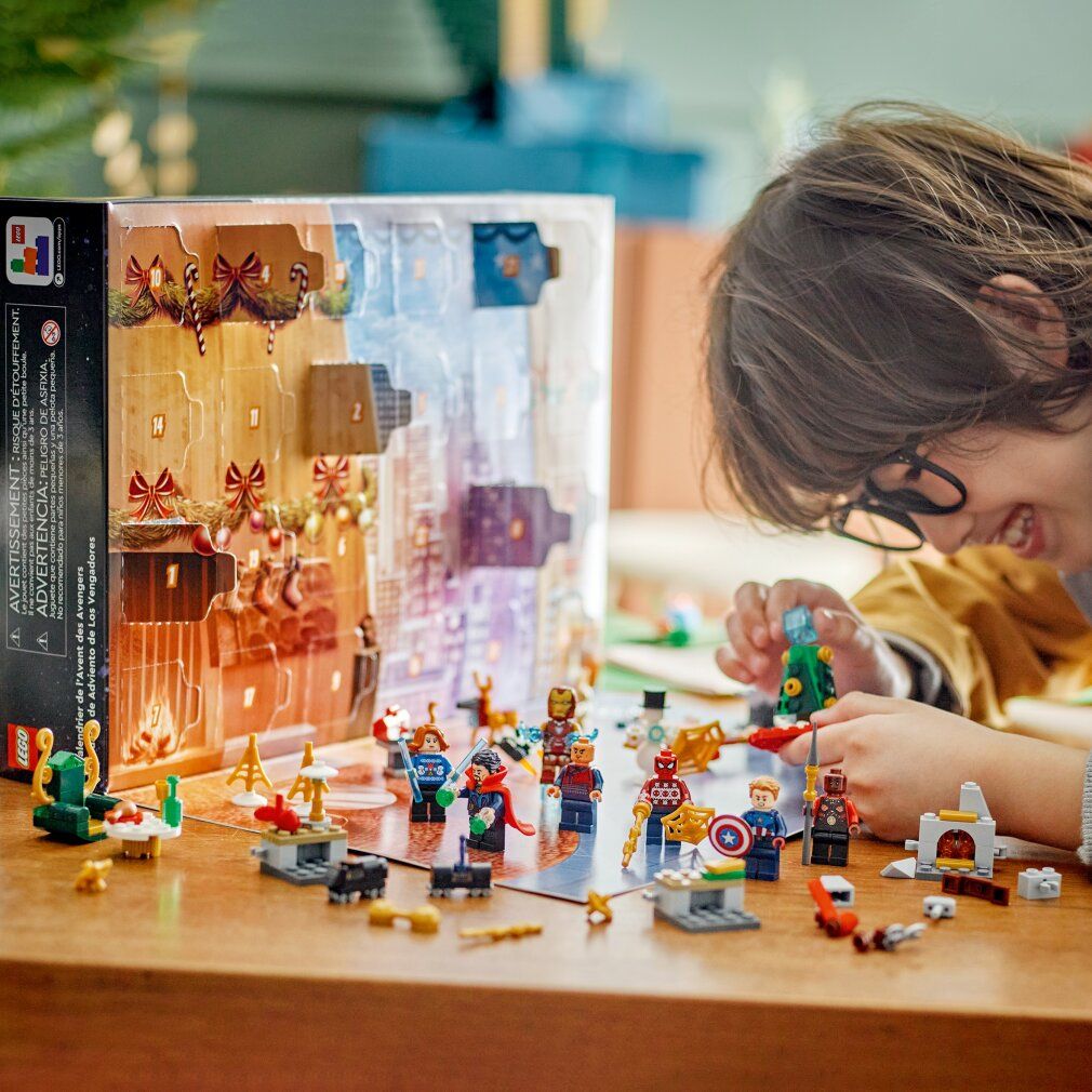 Kind spielt mit LEGO Marvel Adventskalender. Figuren und Szenen auf Tisch. Enthält Iron Man, Spider-Man und Captain America.