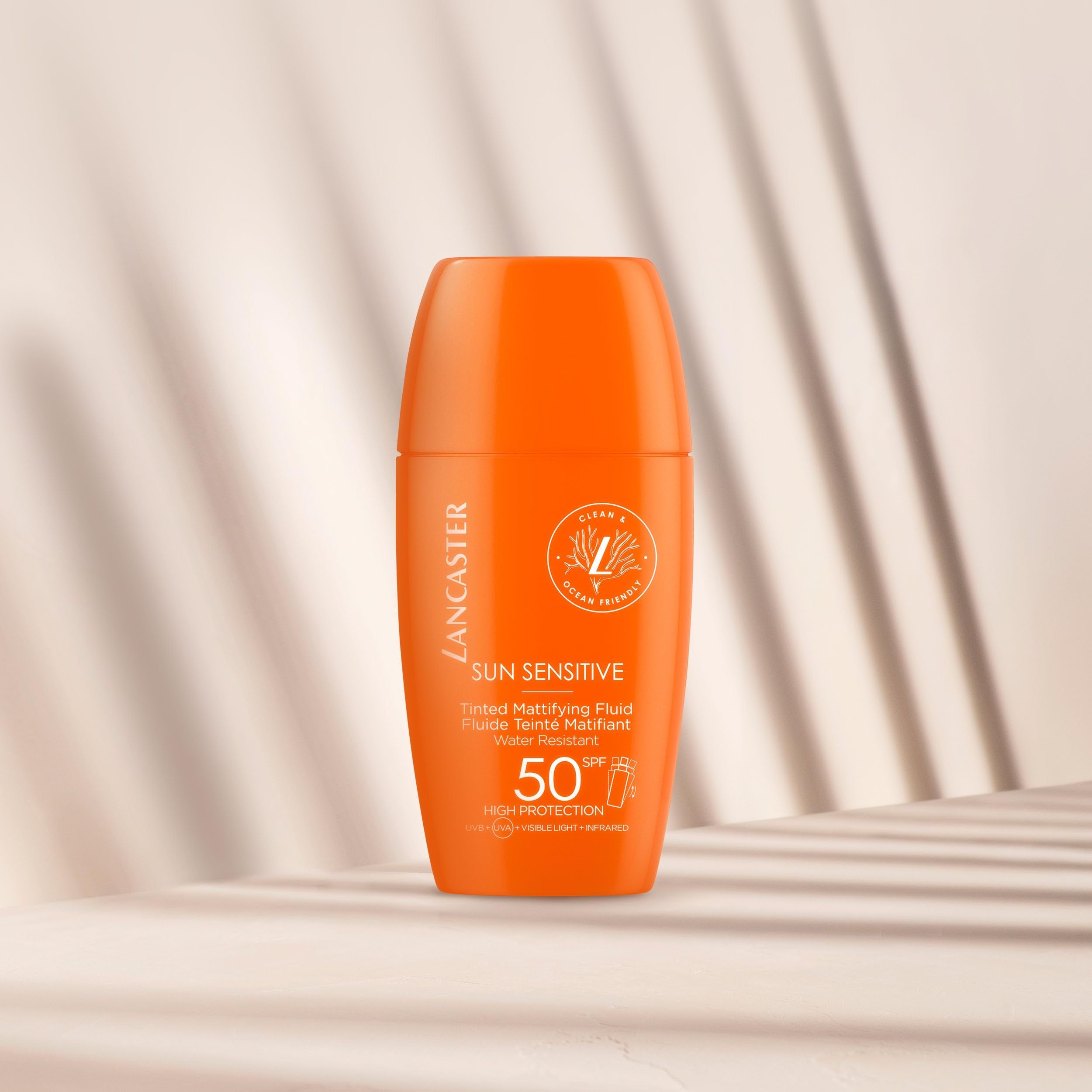 Orangefarbene Flasche von Lancaster Sonnenempfindlicher Tönender Mattierender Fluid SPF50. Text: Sun Sensitive, 50 SPF.