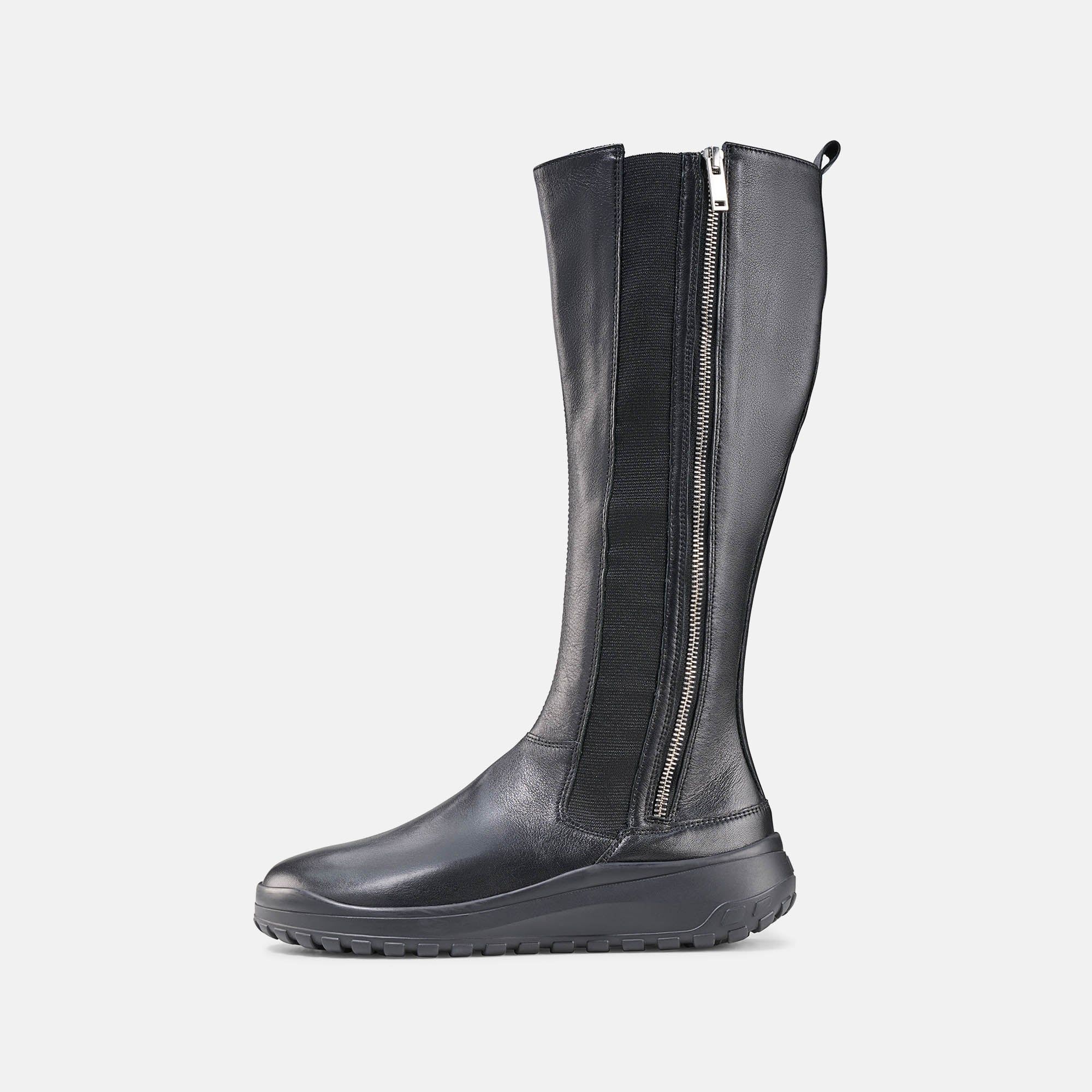 Schwarzer Damenstiefel mit Reißverschluss. Seitliche Gummibandeinsätze. Flache Sohle. Stiefel leicht geneigt.