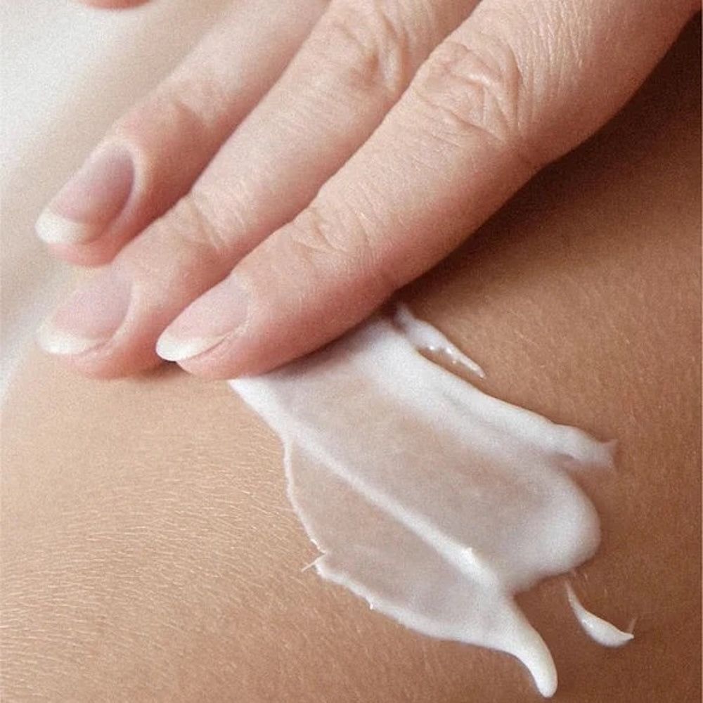 Hand, die Creme auf die Haut aufträgt. Creme ist weiß und hat eine glatte Textur. Haut ist hell.