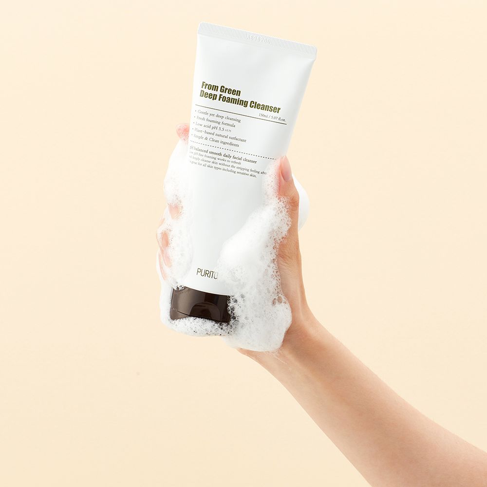 Eine Hand hält eine weiße Tube mit tiefgrünem, schäumendem Reiniger und Schaum.