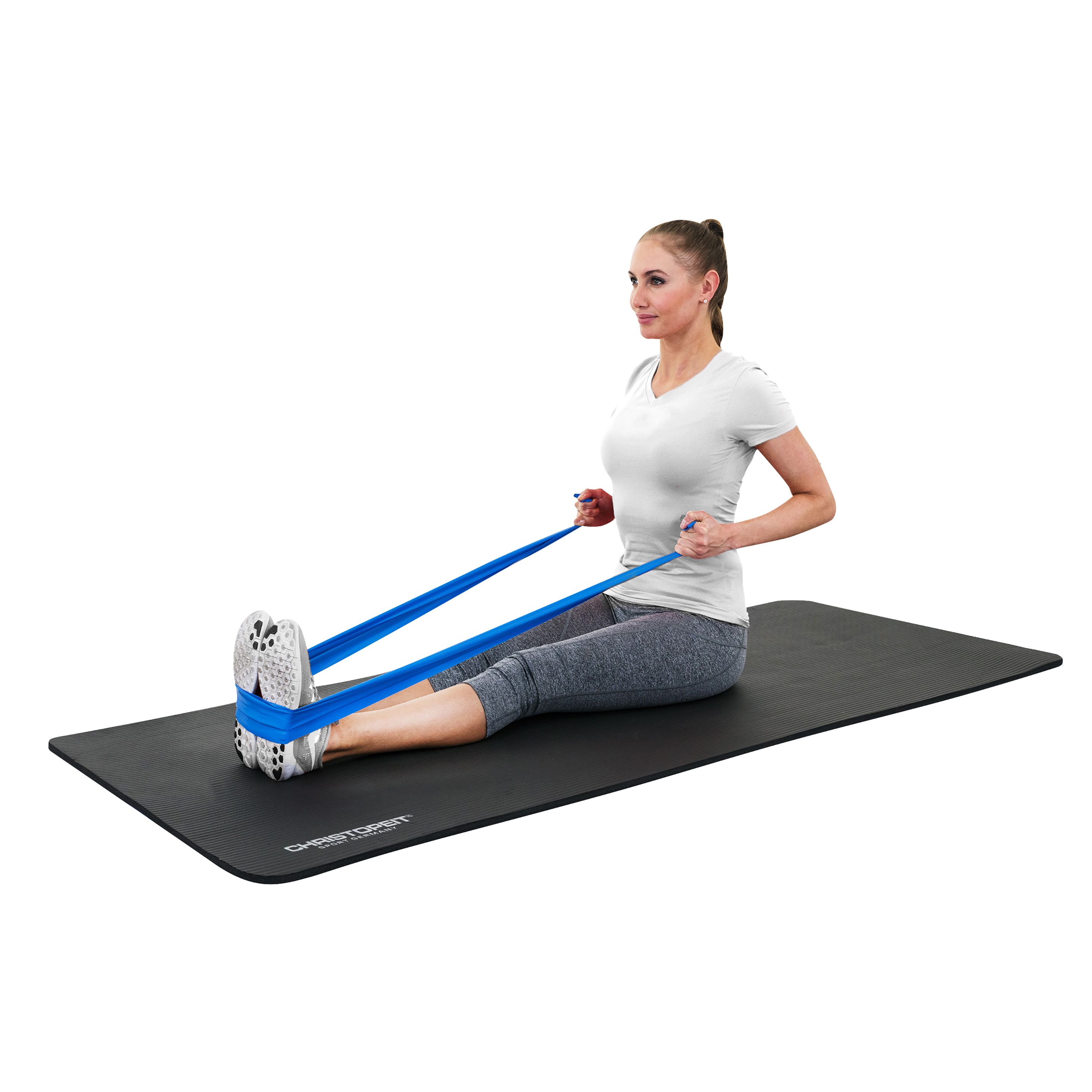 Eine Frau sitzt auf einer schwarzen Matte und trainiert mit einem blauen Gymnastikband. Sie zieht das Band mit den Füßen.