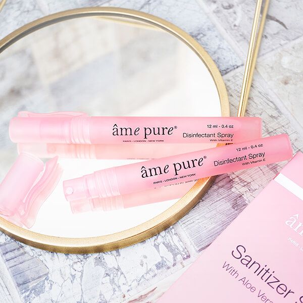Twee roze sprays op een spiegel. Opschrift: âme pure Disinfectant Spray, 12 ml - 0.4 oz, with Vitamin E.