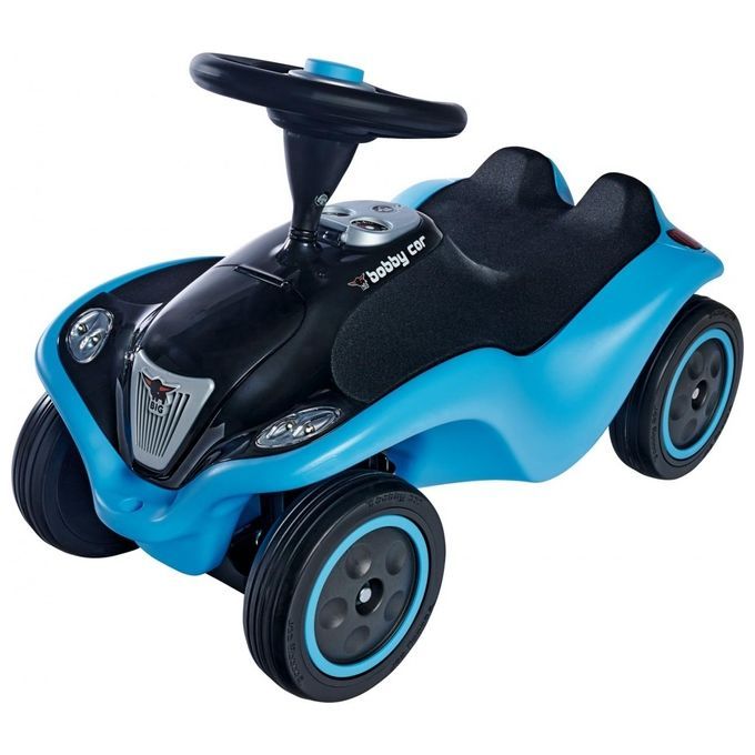 È raffigurata la BIG Bobby-Car NEXT, un'auto per bambini blu e nera. Ha un volante, un sedile e quattro ruote. Il veicolo ha i fari e il logo Bobby Car.