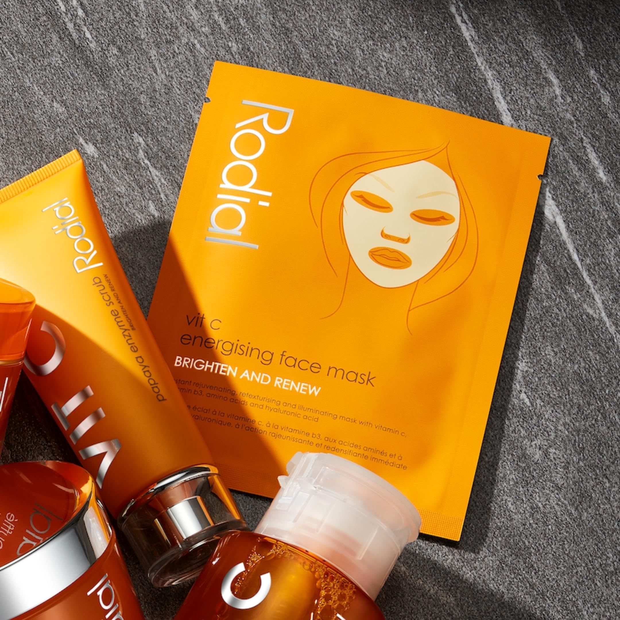 Orangefarbene Verpackung mit Gesichtsskizze und Schriftzug Vit C. Marke Rodial. Text: Energising Face Mask, Brighten and Renew. Umgeben von anderen Produkten.
