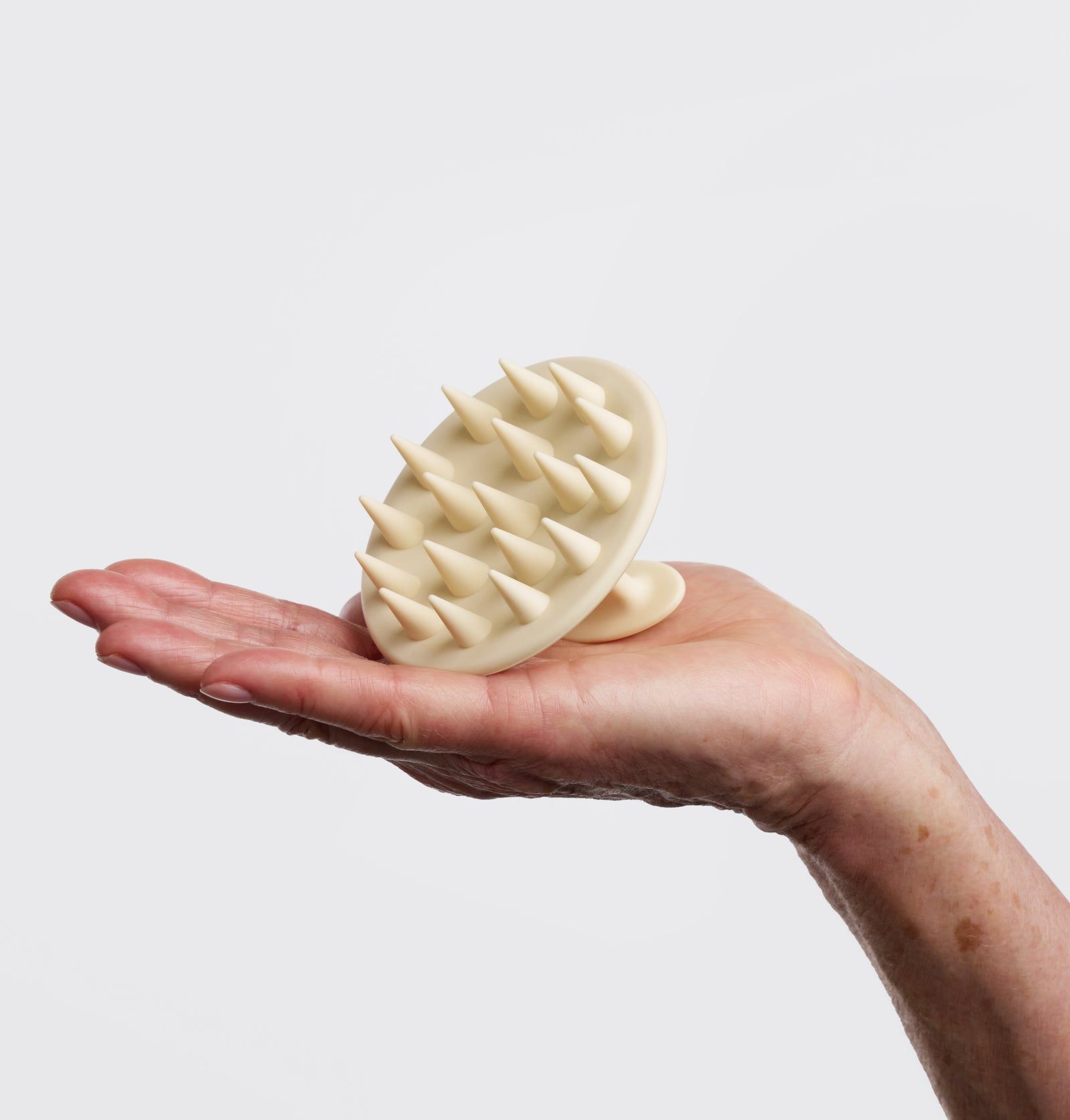 Beige Kopfhautbürste mit kegelförmigen Borsten. Wird in einer Hand gehalten. Runde Form mit Griff.