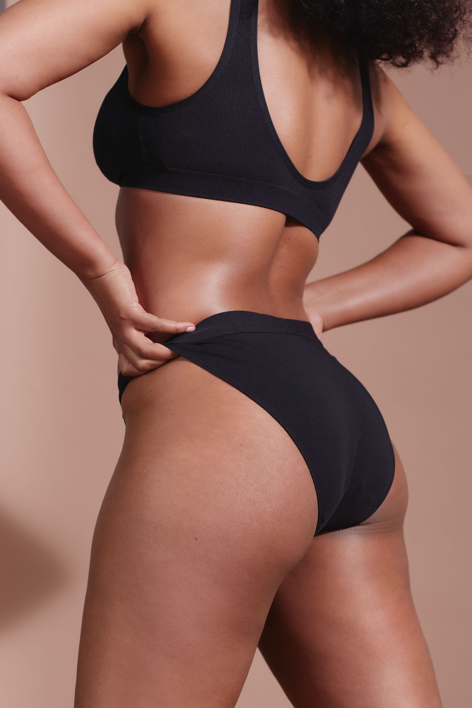 Schwarzer Slip. Frau von hinten, Hände an der Hüfte. Gerippter Stoff.