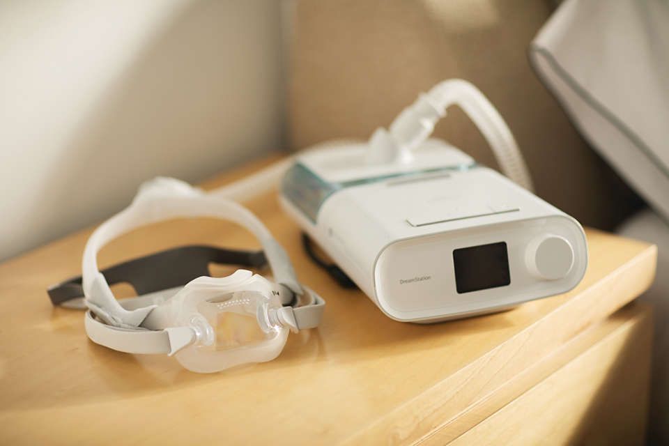 Philips CPAP DreamWear Maske und CPAP-Gerät auf einem Nachttisch.