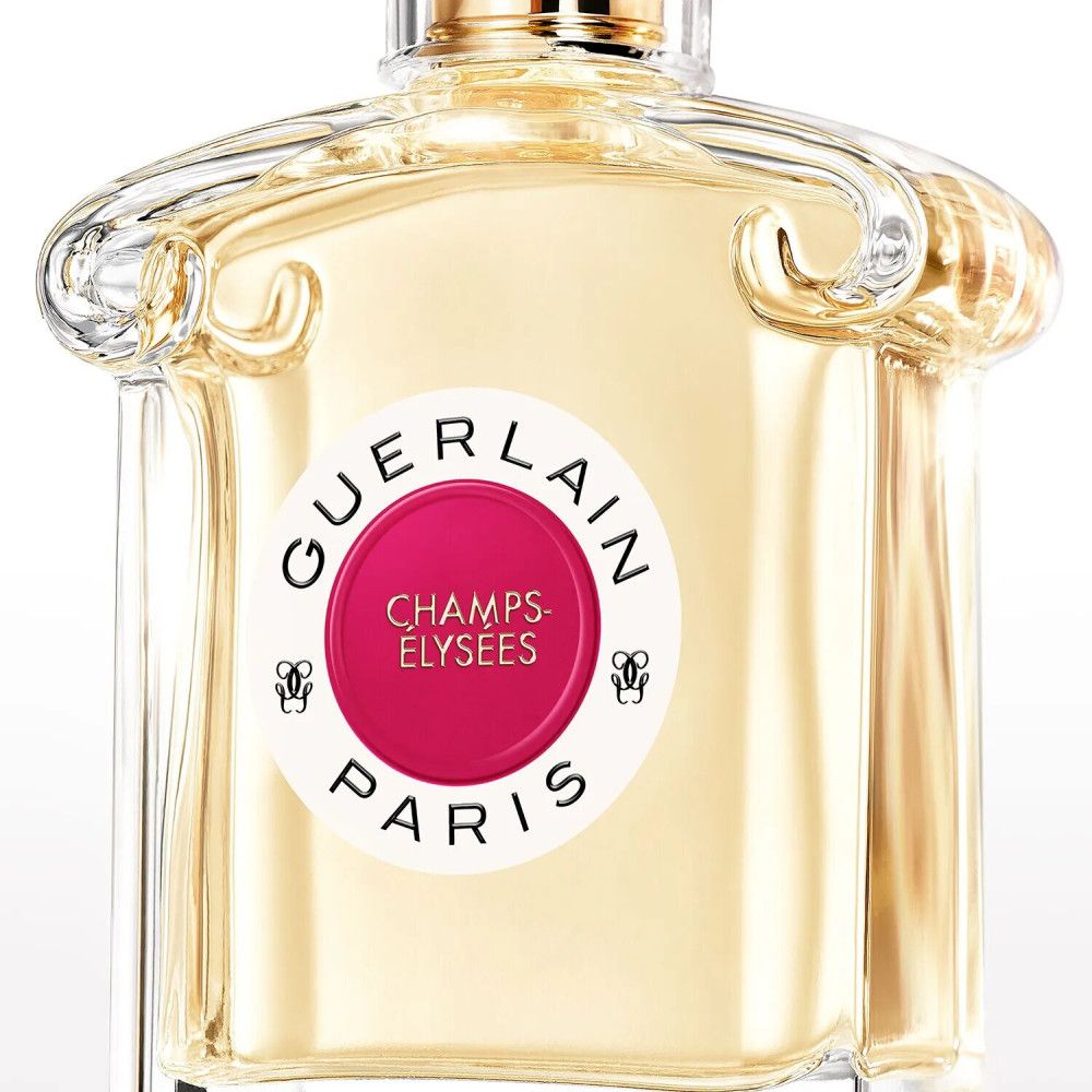 Parfümflakon mit rundem Etikett. Aufschrift: GUERLAIN, CHAMPS-ÉLYSÉES, PARIS. Rosa Kreis. Transparenter Glasflakon mit goldfarbenem Verschluss.