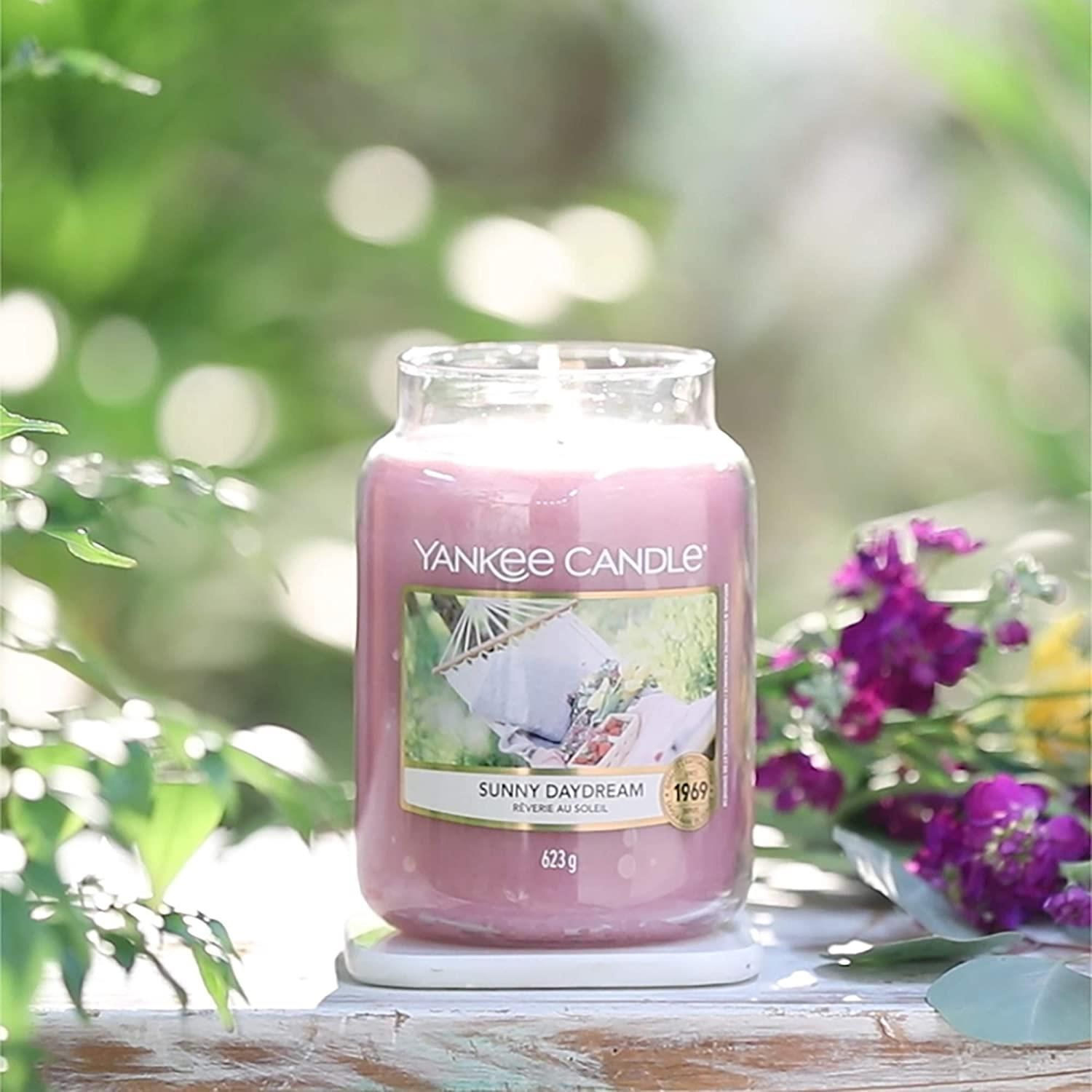 Yankee Candle Duftkerze Sunny Daydream. Rosa Kerze im Glasbehälter. Etikett mit Bild einer Hängematte. Gewicht: 623 g. Auf weißem Untersetzer.