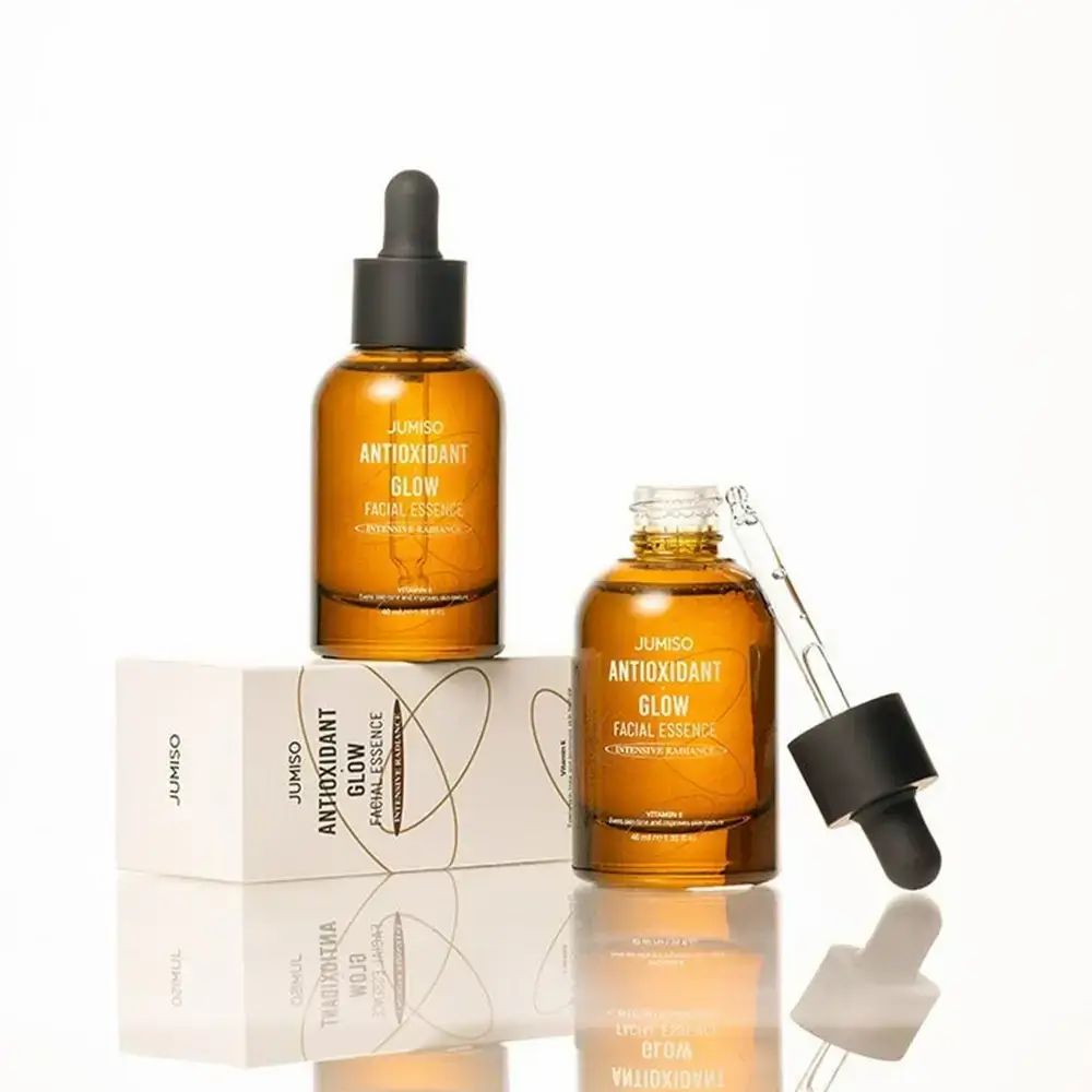 Zwei braune Glasflaschen mit schwarzem Deckel und Pipette. Aufschrift: JUMISO ANTIOXIDANT GLOW FACIAL ESSENCE. Mit Verpackung.