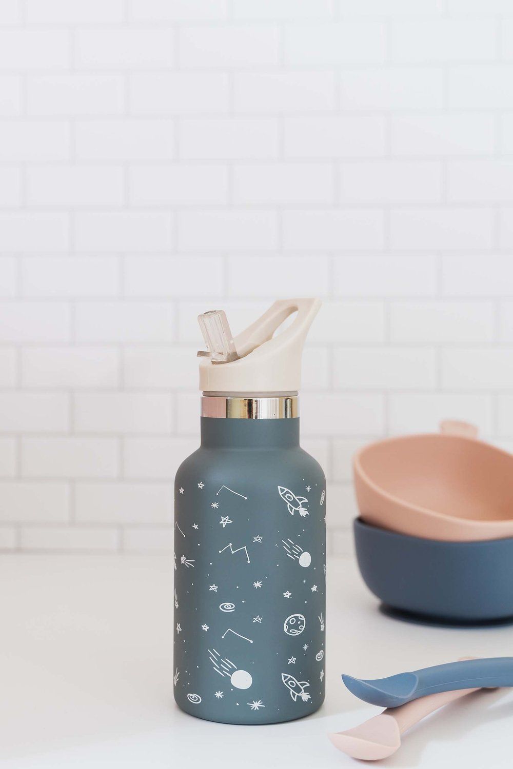 Blaue Edelstahl-Trinkflasche mit Weltraum-Motiv. Weißer Deckel mit Trinköffnung. Auf Tisch.