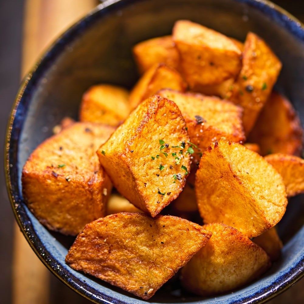 Gebratene Kartoffelstücke in einer blauen Schüssel. Goldbraune Farbe, leicht gewürzt.
