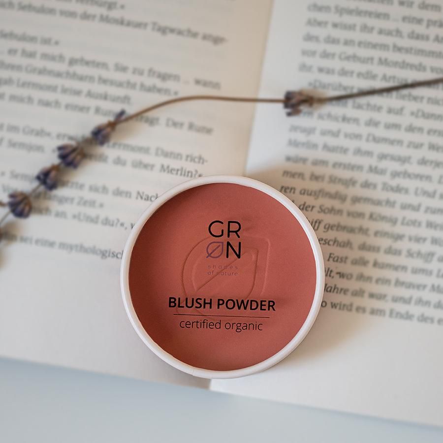 Blush-Puder-Behälter auf einer offenen Buchseite. Aufschrift: GRN, Blush Powder, certified organic.