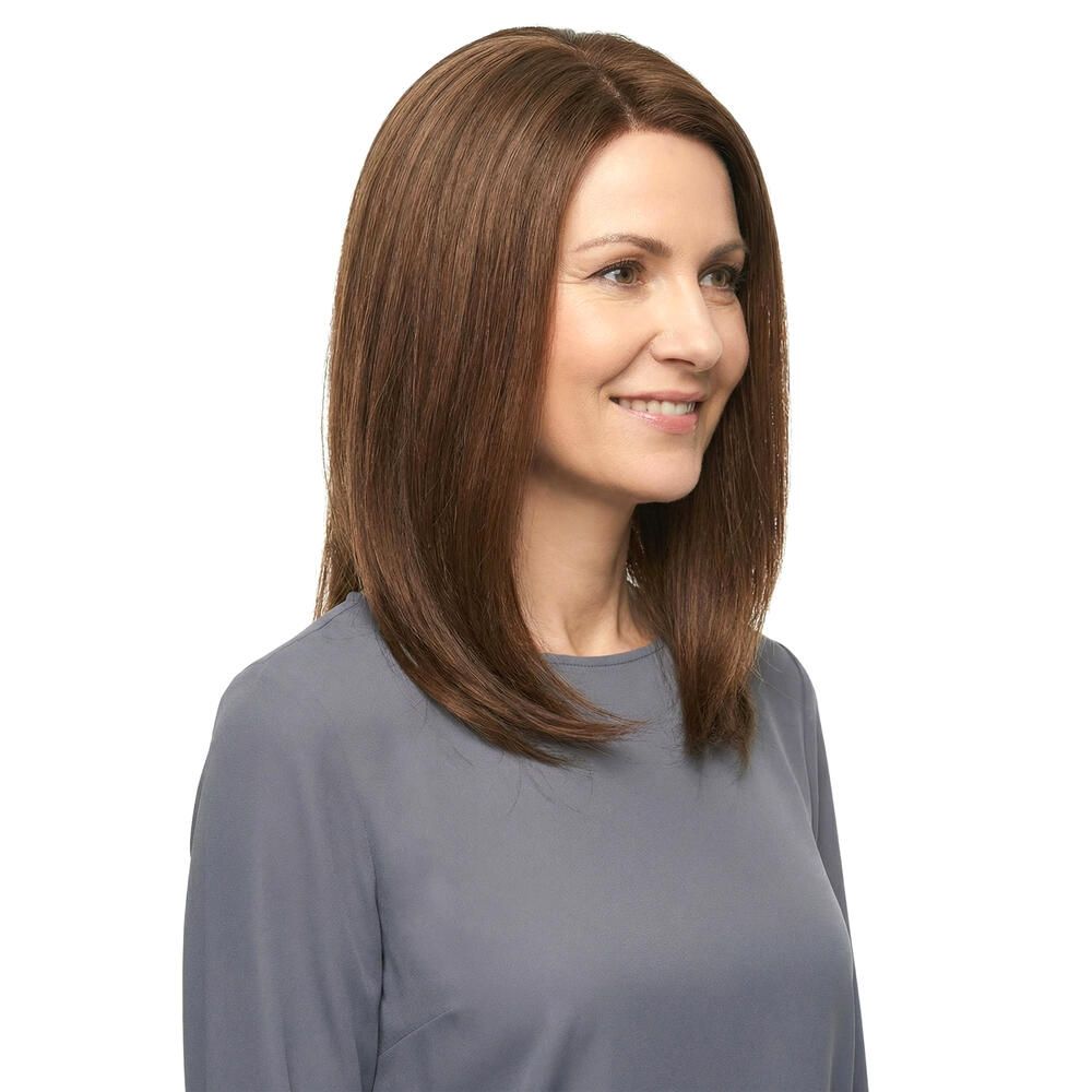 Frau mit brauner Perücke, schulterlang, leicht gewellt. Trägt graues Oberteil. Blick nach vorne.
