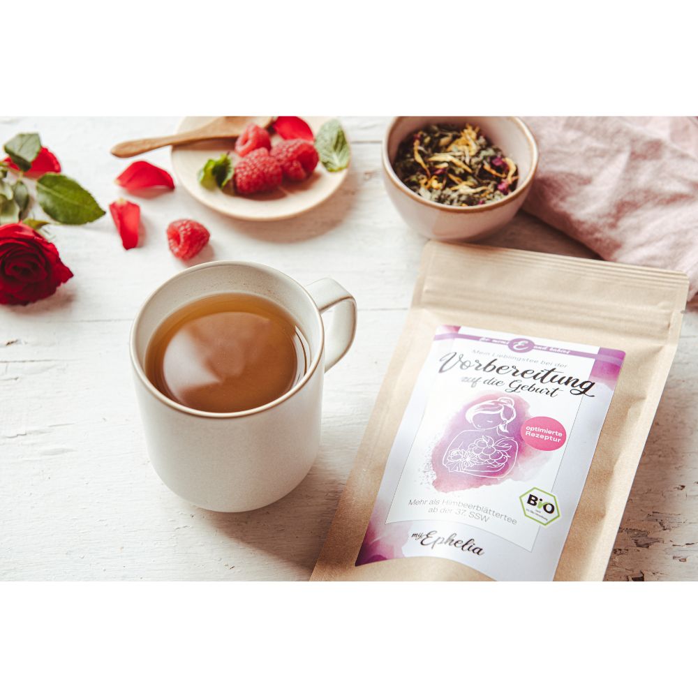 myEphelia Geburtsvorbereitungstee mit Tasse Tee, Himbeeren und Rose. Brauner Papierbeutel mit Bio-Siegel.