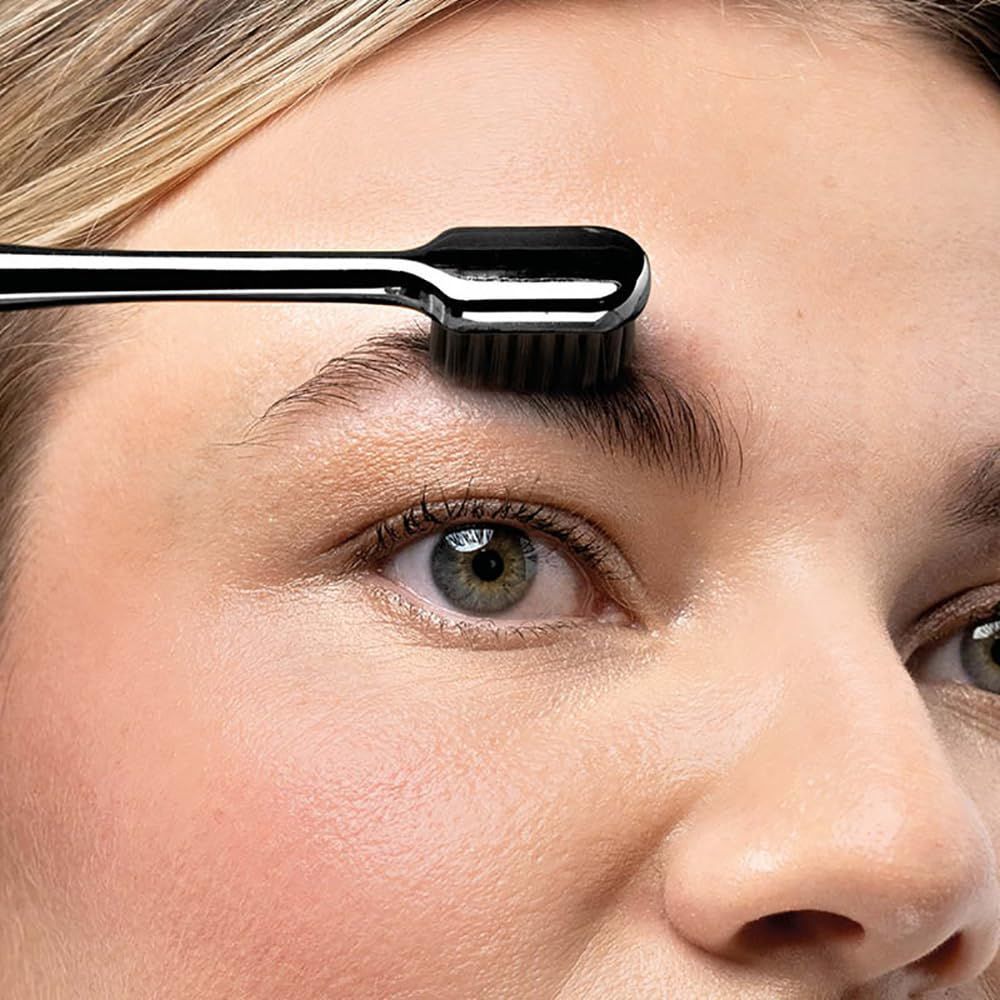 Nahaufnahme einer Frau mit Augenbrauenbürste. Bürste auf Augenbraue. Schwarze Bürste mit M2 BEAUTÉ-Logo.