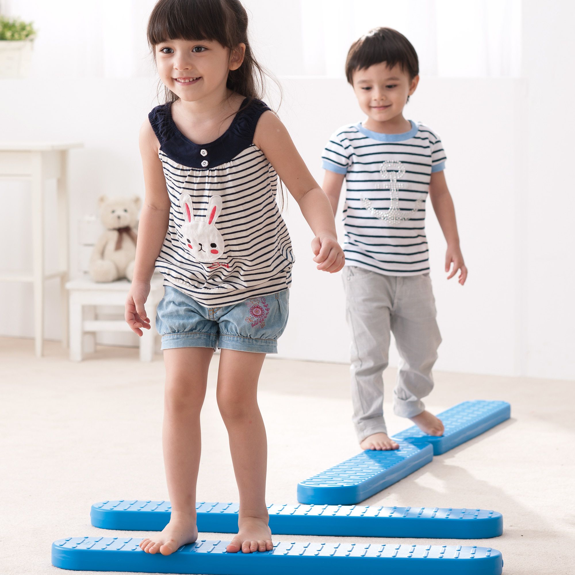 Zwei Kinder balancieren auf blauen Balance Brettern. Ein Mädchen und ein Junge gehen barfuß. Helle Umgebung.