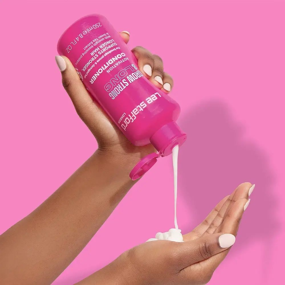 Hände halten eine rosa Flasche. Produkt wird in die Handfläche gegossen. Produktname: Grow Strong & Long Conditioner.