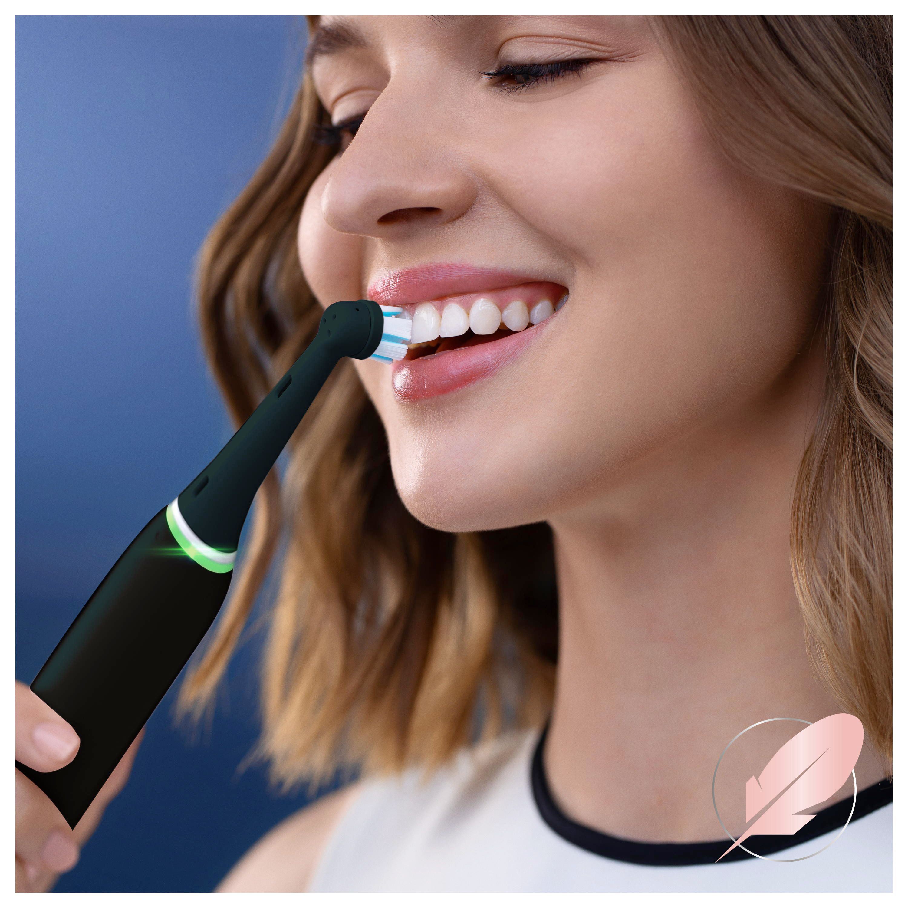 Frau putzt sich die Zähne mit einer schwarzen elektrischen Zahnbürste. Bürstenkopf mit blauen Borsten.