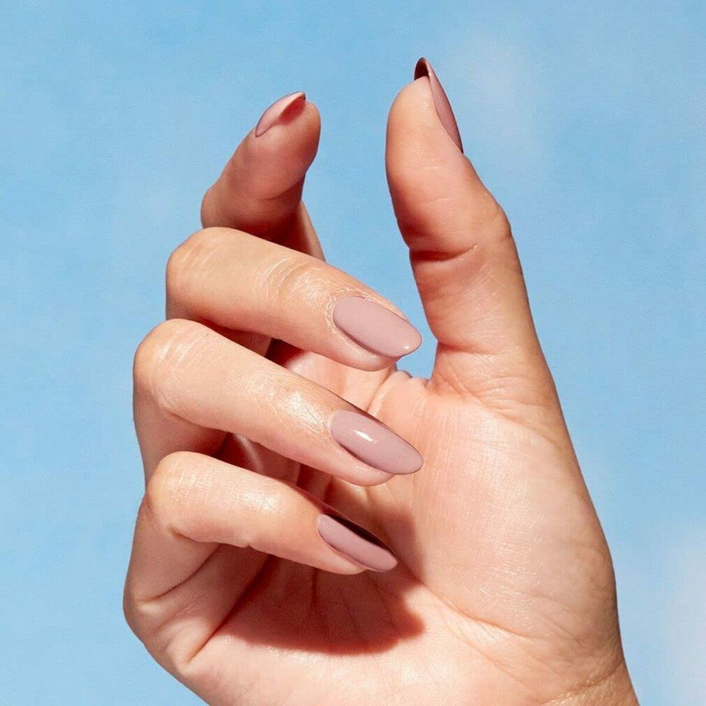 Hand mit lackierten, ovalen Nägeln in Rosa. Blauer Hintergrund.